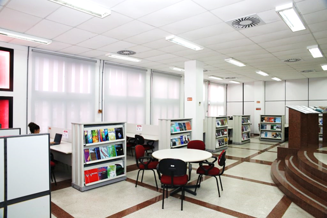 Sala de leitura com mesas e estantes cheias de livros.
